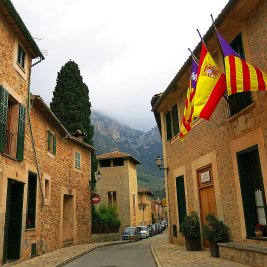Panorámica del pueblo de Deià en Mallorca, con sus casas de piedra ocre en una colina coronada por la iglesia y montañas al fondo
