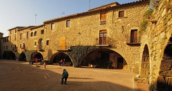 Plaza porticada medieval de Monells con arcos de piedra y casas doradas del Baix Empordà