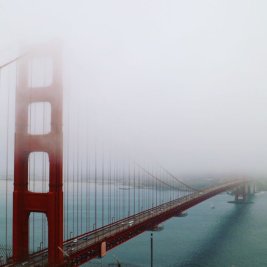 Gran puente colgante sobre el agua envuelto parcialmente en niebla